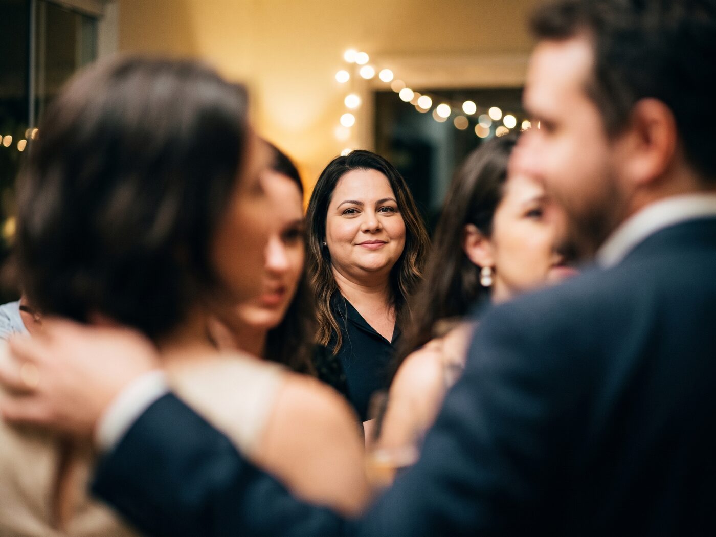 Mulher num vão entre convidados numa festa, meio encoberta pelas outras pessoas