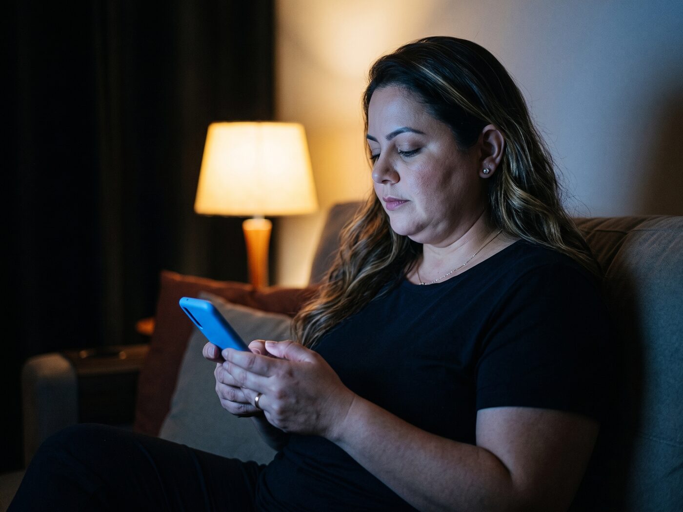 Mulher em casa à noite, olhando um convite na tela do celular